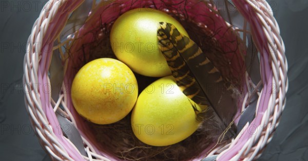 Colorful painted marble shiny Easter eggs in a basket with delicate feathers close-up. Nest with straw, Easter decoration on the table