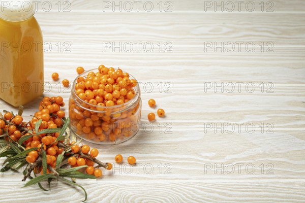 Sea buckthorn healthy drink in bottle, ripe berries in glass jar and branches with leaves top view on white wooden rustic background, great for skin, heart, vessels and immune system. Copy space, food photography, food photography