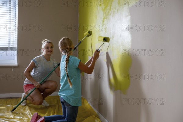 Two kids are joyfully and creatively painting a wall a bright yellow color, showcasing their teamwork and imagination