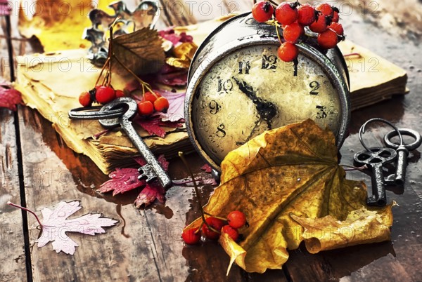 Od clock book and the keys on the wet table strewn with autumn leaves.Photo tinted
