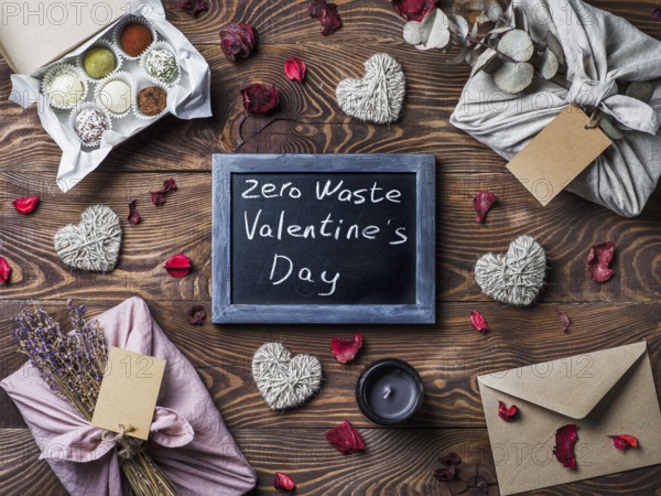 Zero waste Valentine's Day concept. Eco-friendly gift cloth wrapping in Furoshiki style, homemade sweets as gift ideas and chalkboard with Zero Waste Valentine's Day letters on brown wooden background
