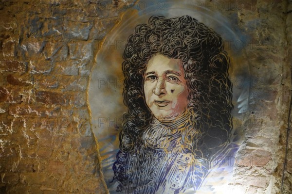 MAUSA VAUBAN, Museum of Urban Art and Street Art, Neuf-Brisach Fortress, France, Europe, Graffiti of a portrait of a historical figure with curly hair on a brick wall with yellow and blue accents