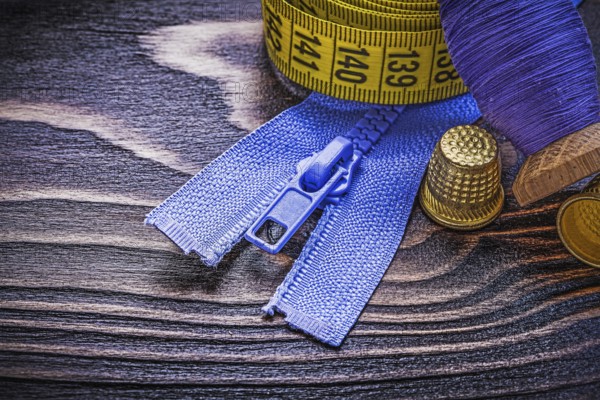 Vintage spool of thread measuring tape thimbles zip fastener on wooden board needlework concept