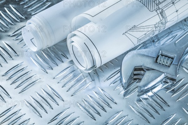 Rolled construction plans adjustable spanner on channeled metal background