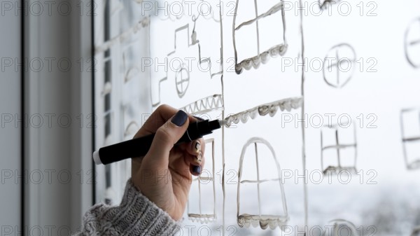 Female hand draws christmas holidays decoration painted on window glass. New Years scenery. city buildings garlands lights. hygge, decoration and christmas concept. festive string at home