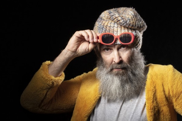 An elderly man with a grey beard wearing a knitted hat and a bright yellow fur coat. Fashionable man on a black background