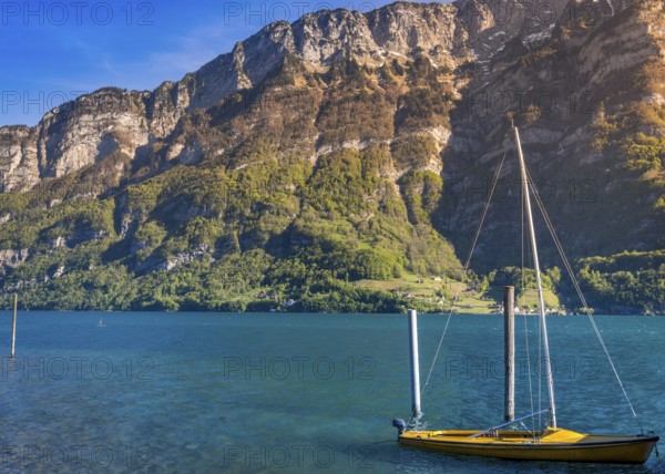 Image taken in the Murg Ost village, Switzerland, presenting a small boat on the Walensee lake in the morning sunlight, surrounded by the Swiss Alps mountains