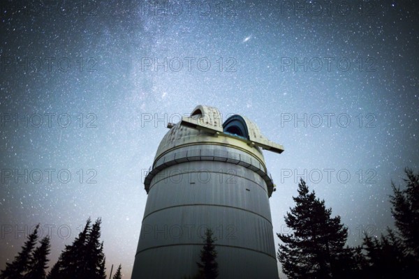 Rozhen astronomical observatory under the night sky stars. Blue sky with hundreds of stars of the Milky way. Observatory in a pine trees forest in the mountain. Vignetting