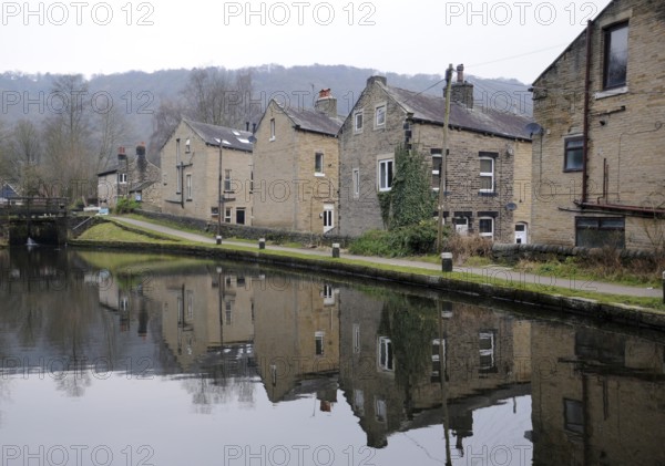 Houses alongside the rochdale canal in hebden bridge with reflections in the water and lock gates in the distance