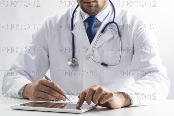 Close up of male doctor hands using tablet computer. Physician in white medical uniform with stethoscope sitting at desk. Modern technology in examination and diagnosis. Medical digital application