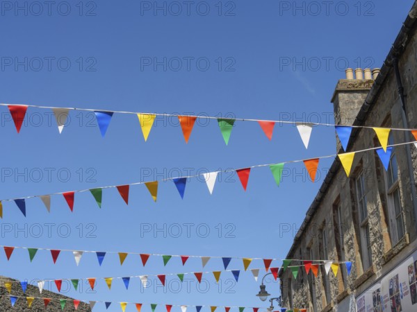 Colourful flags hang over a street corner between historic buildings under a cloudless blue sky, Lerwick, Shetland, Scotland, United Kingdom