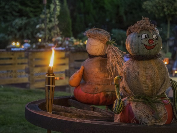 Two pumpkin sculptures sitting on a wooden wheel, illuminated by a burning torch in the evening garden, borken, münsterland, Germany