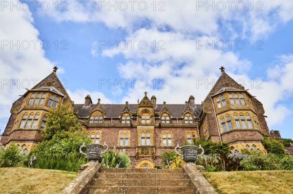 Large building with symmetrical architecture, surrounded by garden and staircase under blue sky. Knightshayes, Tiverton, Devon, England, Great Britain, United Kingdom