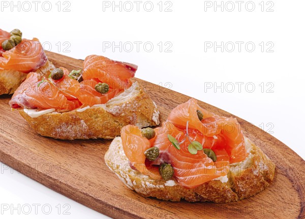 Food, Delicious canapés topped with smoked salmon and capers rest on a wooden platter. The vibrant colors of the salmon contrast nicely with the rustic bread, creating an appetizing sight