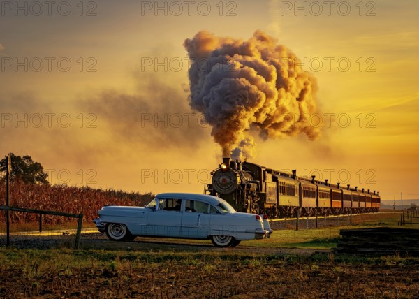 A View of an Antique Steam Passenger Train Approaching at Sunrise With a Full Head of Steam and Smoke Traveling Thru Farmlands With An Antique Car Waiting for it to Passes