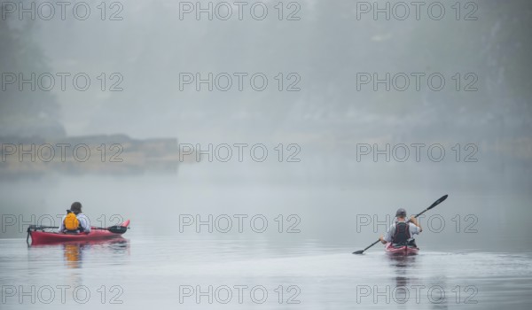 Kayakers navigate a calm waterway on a foggy day in Lunenburg, Nova Scotia, Canada, North America