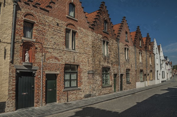 Brick facade of old houses with a blue sunny sky in an empty street of Bruges. With many canals and old buildings, this graceful town is a World Heritage Site of Unesco. Northwestern Belgium