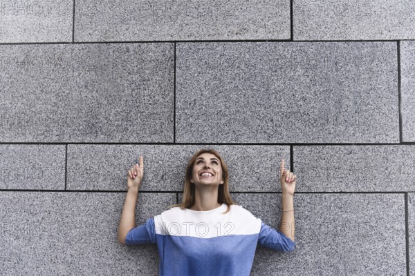 Cheerful girl at the street, show a big sale, or nice offer. Advertise concept. People, travel and tourism, woman on city street and girl show with her fingers something over gray wall background