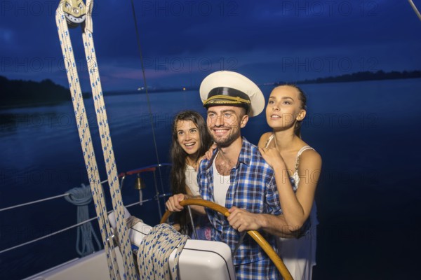 Captain with girls on the yacht. Night cruise on the yacht. Friends traveling by yacht on the river. Holiday on a yacht