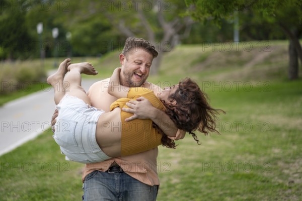 Man with happy expression carrying his girlfriend in his arms in a park