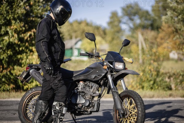 Biker in black helmet standing by an off-road bike in the countryside