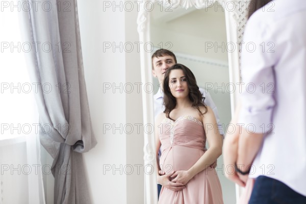 Portrait of the pregnant woman and young man together indoors