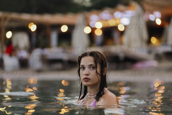 Woman in a pool during evening with bokeh lights in the background, creating a calm atmosphere