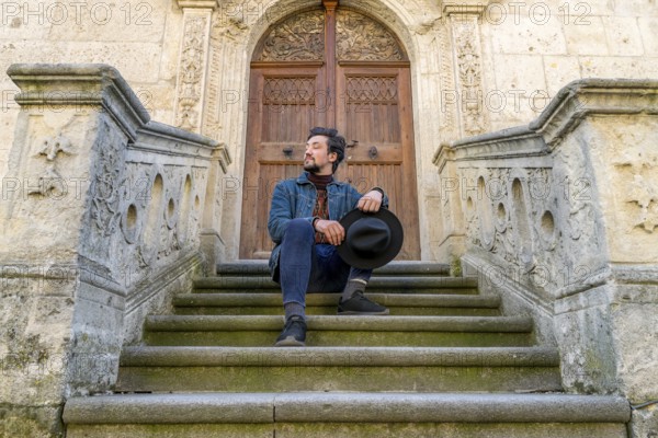 Portrait of a young man sitting against a beautiful old medieval cathedral door. A man in front of a an old architecture church entrance door in Alba Iulia, Romania