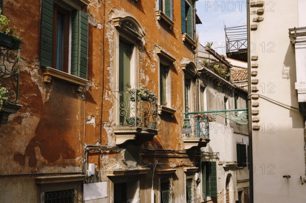 Close-ups of building facades in Venice, Italy. Green wooden door at bottom of brick house. Balcony with a forged fence. An old street lamp on the wall of an apartment building