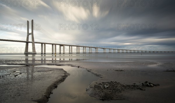 Vasco da Gama Bridge at sunset with dramatic cloudy sky in Lisbon Portugal. Long exposure photograph