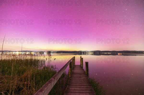 A wooden footbridge leads over a calm lake under a sky with aurora borealis, Reichenau, Lake Constance, Baden-Württemberg, Germany