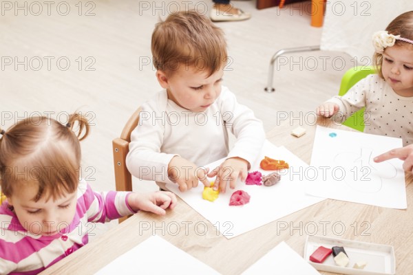 The teacher helps the girl to make a figure plasticine on the table