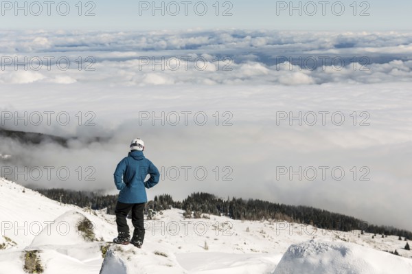 Freestyle skier is looking from the top of a peak of Vitosha mountain covored in clouds. He is participating in an freestyle competition of skiers and snowboarders