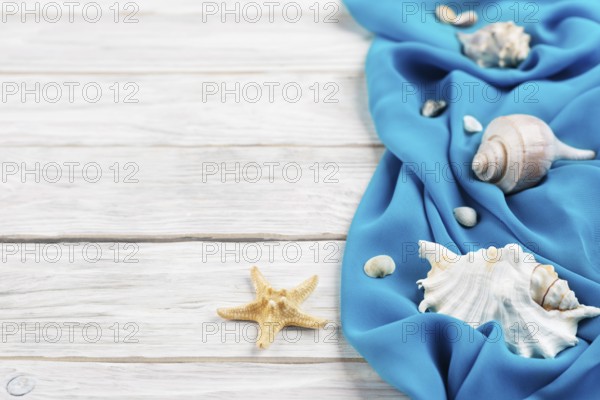 Seashells, blue fabric and starfish on white planks vacation planning background flat lay with copy-space