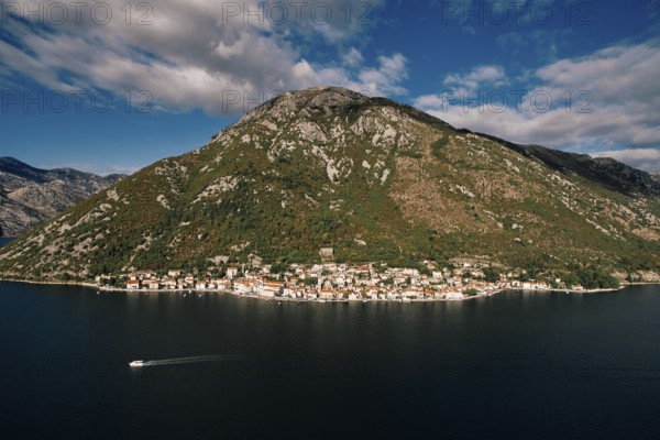Boat sails along the Bay of Kotor against the backdrop of the coast of Perast at the foot of the mountains. Montenegro. Aerial view.