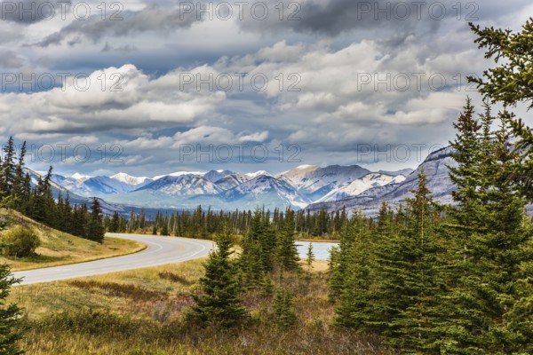 The road to distant snow-capped mountains in the Rockies of Canada. Rocks and lakes under flying clouds. Concept of active and ecological tourism