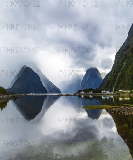 Magic country of fantastic heroes. New Zealand. Storm clouds cover the sky. Mirror-smooth water of the Milford Sound fjord reflects mountains. Concept of exotic, active and photographic tourism