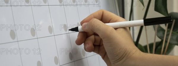Female hand writing with marker on Monthly PLANNER. Magnetic board with the days of the month. Place to enter important matters schedule. Concept for business planning. Whiteboard Planner magnetic monthly template. Interior of freelancer workplace