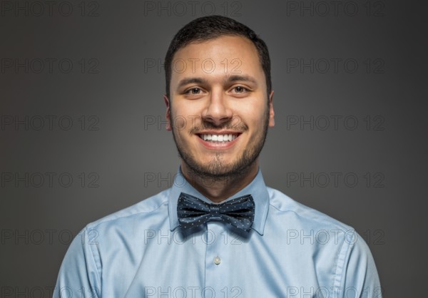 Portrait of happy smiling young man in blue shirt and butterfly tie isolated over gray studio background. Closeup