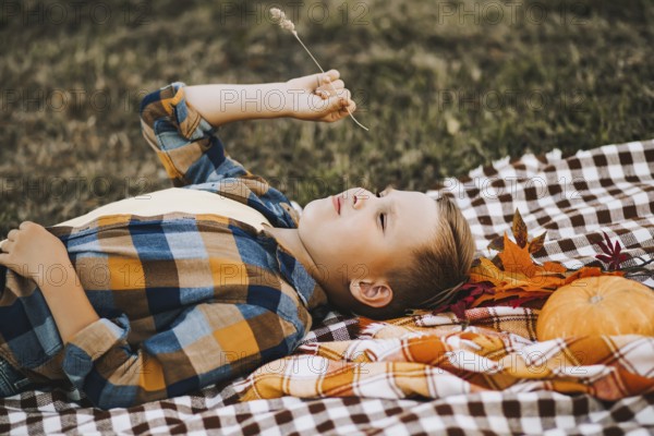 Kid boy lies near a river, pond or lake and smiling. Autumn season. Happy childhood