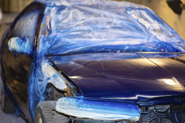 A blue car partially covered with plastic sheeting in a workshop setting