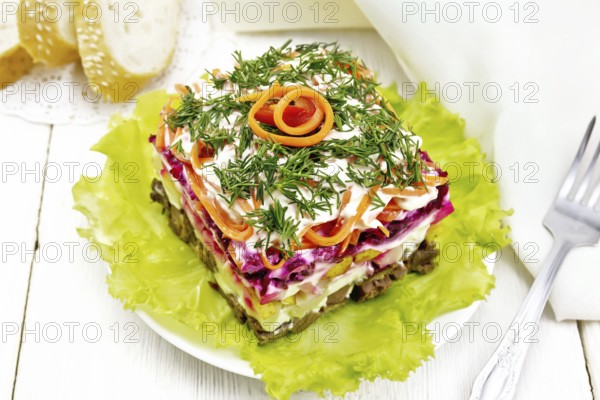 Puff salad with beef, boiled potatoes and beets, pears, spicy Korean carrots, seasoned with mayonnaise and garnished with dill on a green lettuce in plate on white wooden board background
