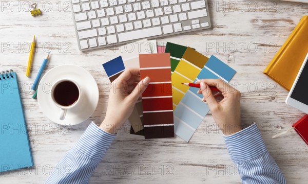 Web designer choosing colors from swatches at wooden desk. Office workplace with computer keyboard and cup of coffee. Designing user interface of mobile application. Coloristics in visual design