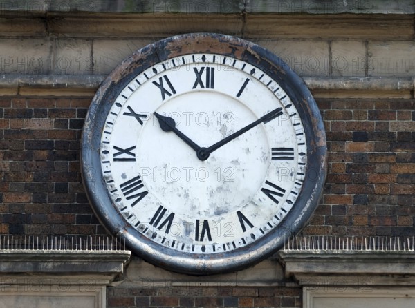 Old round clock on the brick wall of a building with roman numerals with hands at ten past ten
