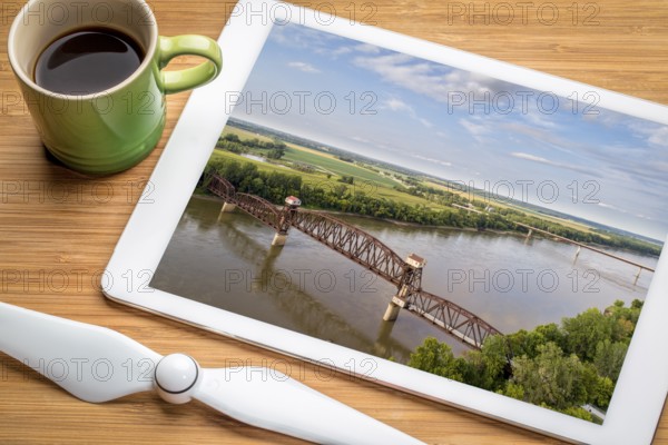 Historic railroad Katy Bridge over Missouri River at Boonville - reviewing aerial image on a digital tablet with a cup of coffee