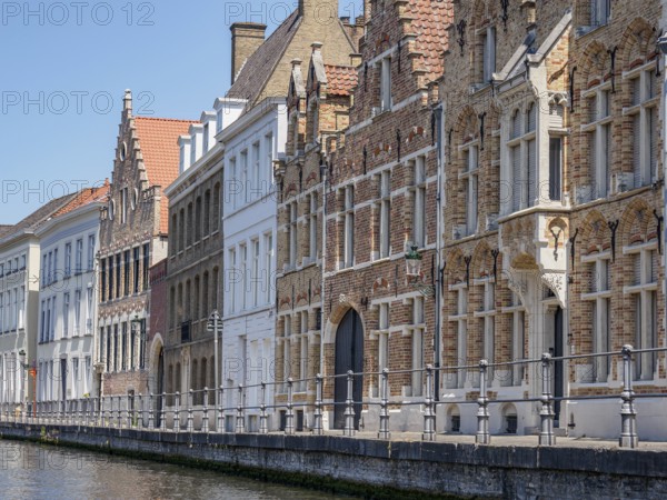Historic buildings on the banks of a canal with striking Gothic facades and a clear blue sky, Bruges, Belgium