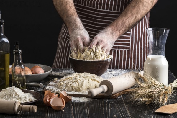 A handful of flour with egg on a rustic kitchen. Against the background of men's hands knead the dough. Ingredients for cooking flour products or dough bread, muffins, pie, pizza dough . Copy space