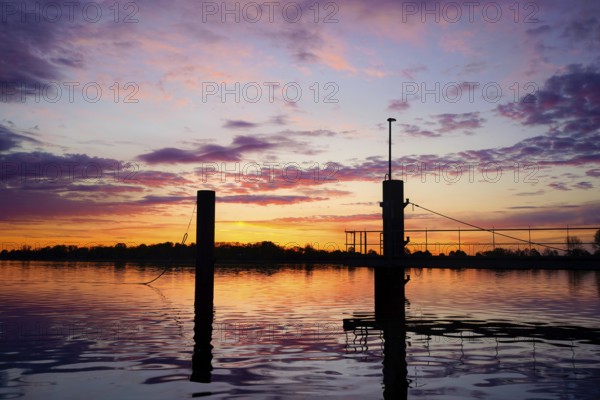 Bollard on the water in a pink morning sky with atmospheric reflection at dusk, An der Kaje / Weser, 26919 Brake-Germany