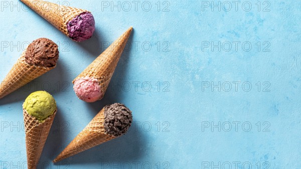 Various ice cream scoops in cones with copy space. Colorful ice cream in cones chocolate, strawberry, blueberry, pistachio or matcha, biscuits chocolate sandwich cookies on blue background. Top view