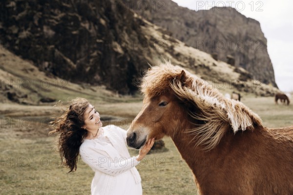 Destination Iceland wedding photo session with Icelandic horses. A bride in a white dress strokes a horse's nose. Hair and mane develop in the wind